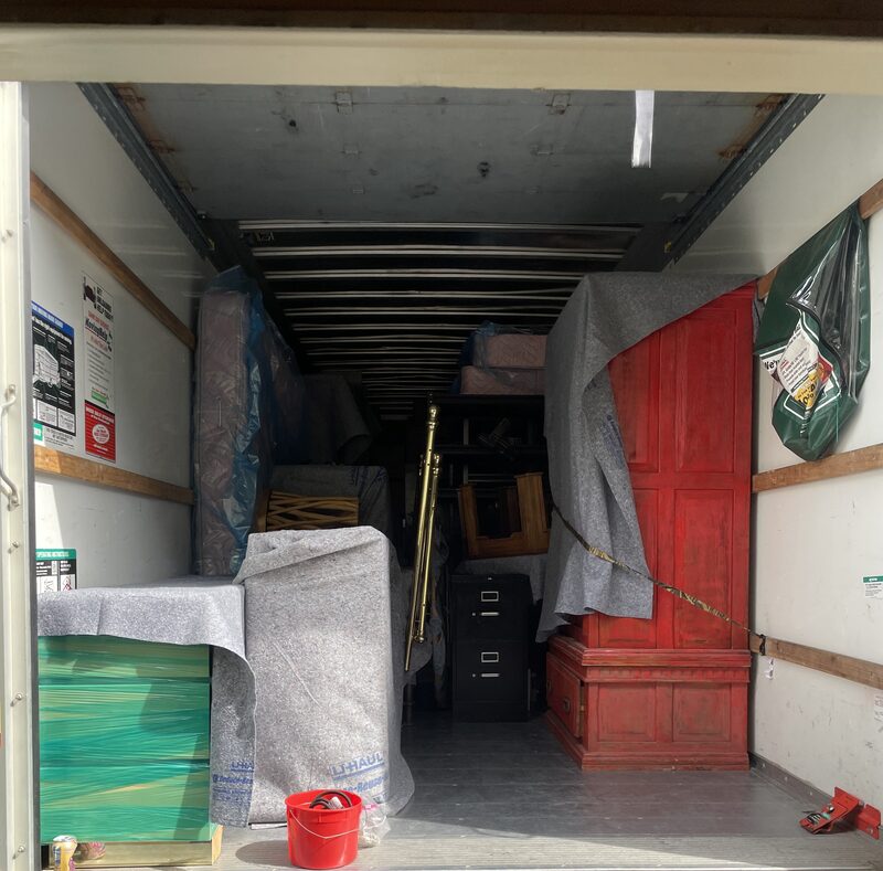 An antique red dresser pad-wrapped and standing upright in a loaded moving truck