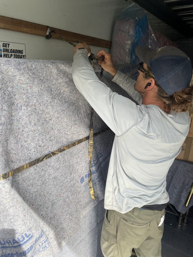 A Big Why Movers crew member ratchet-strapping a blanket-wrapped piece of furniture inside the truck