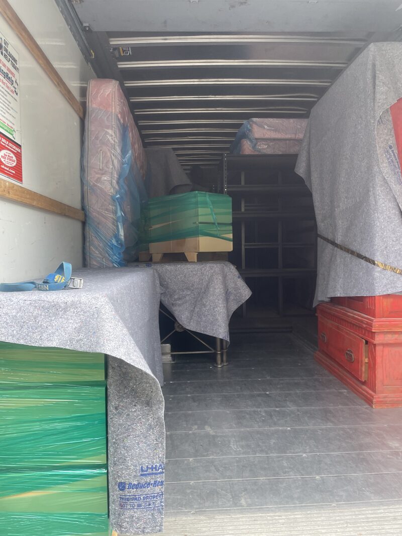 Furniture under moving pads and shrink wrap stacked inside a moving truck